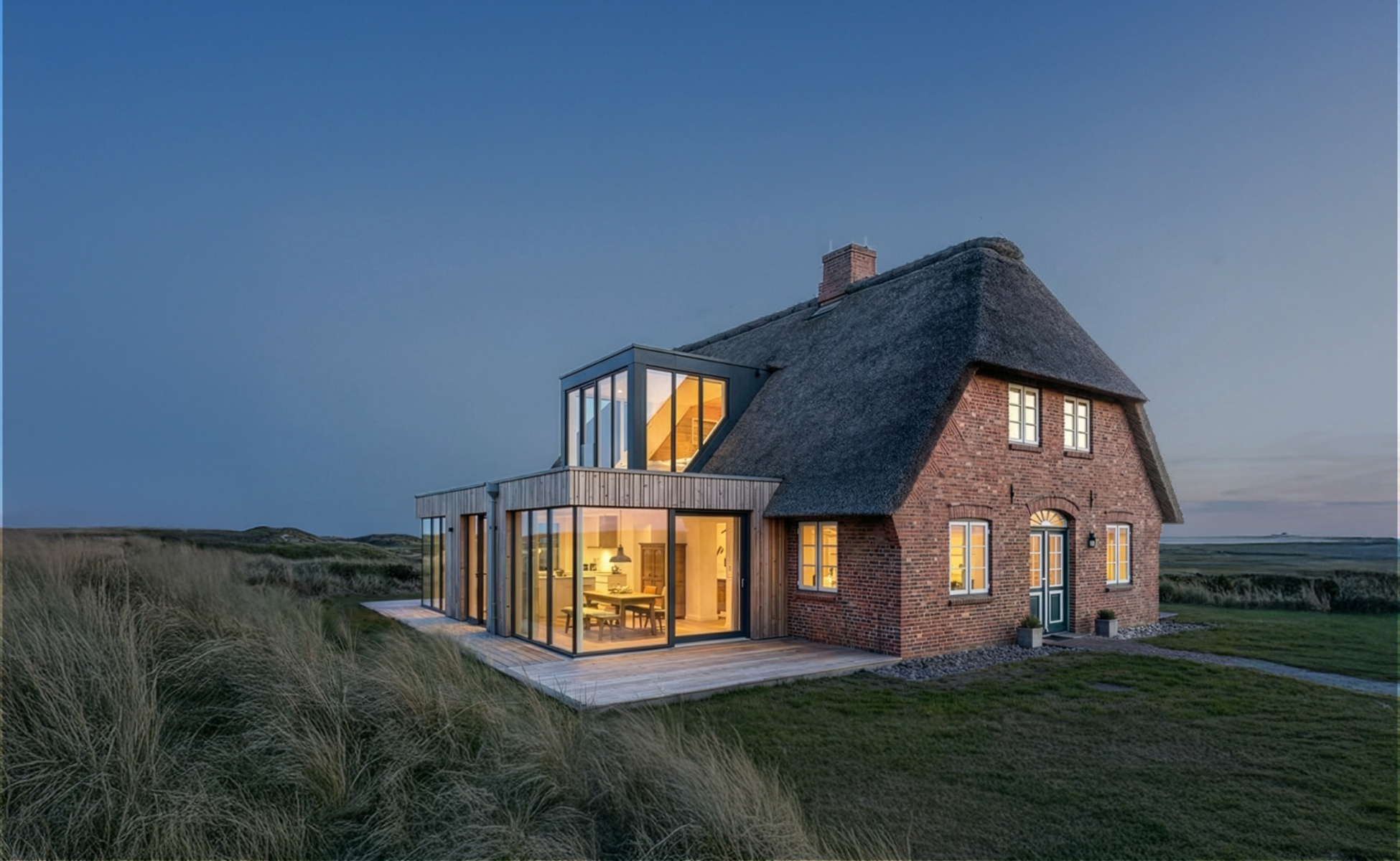 Reetgedecktes Haus mit modernem Glasanbau in einer Küstenlandschaft bei Abendlicht